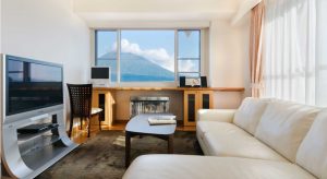 A room with a large white couch and TV with a view of the mountains